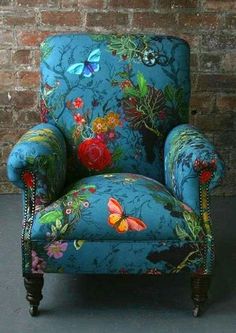 an upholstered blue chair with colorful flowers and butterflies on the armrests