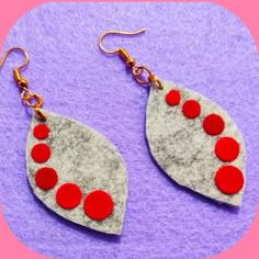 two pairs of earrings with red and white designs on purple felt, sitting on a pink background