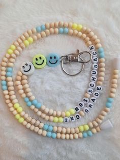 three beaded bracelets with smiley faces and letters on them, sitting on a white furnishing