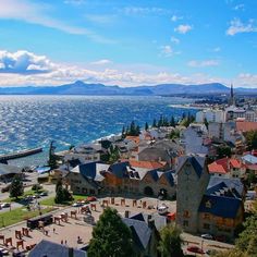 an aerial view of a town by the water with mountains in the background and blue sky