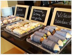 sandwiches are displayed on trays at a buffet table with chalkboard menus behind them