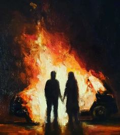 two people standing in front of a fire with a car on the road behind them