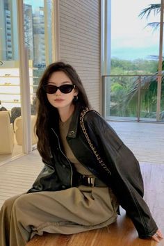 a woman sitting on top of a wooden table wearing sunglasses and a black leather jacket