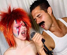 a man and woman with red hair are singing into microphones while another person has his face painted