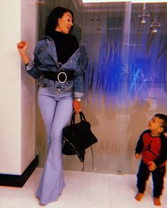 a woman standing next to a little boy in front of a glass wall and holding a handbag