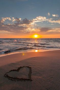 a heart drawn in the sand at sunset