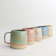 four different colored coffee mugs sitting next to each other on a white table top