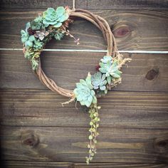 a wreath with succulents and greenery is hanging on a wooden wall