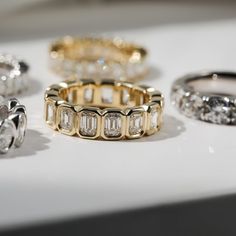 five different types of rings on display in a store window sill, including one with an emerald cut diamond and the other with smaller round diamonds