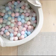 a bowl filled with pastel colored balls sitting on top of a wooden floor next to a rug