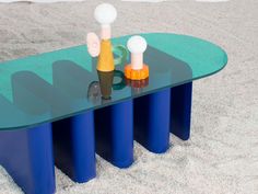 a glass table with three different colored vases on it and sand in the background