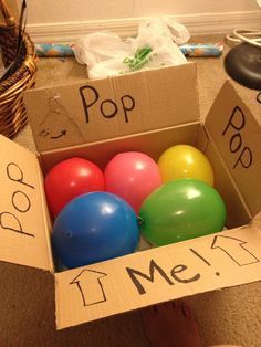 a cardboard box with balloons in it on the floor next to a person's feet