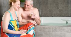 a man and woman sitting in front of a bath tub drinking wine together, smiling at each other