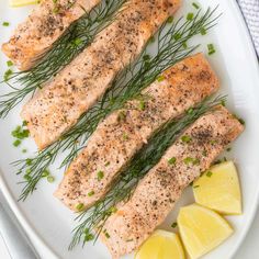 three salmon fillets on a white plate with lemon wedges and chives around them