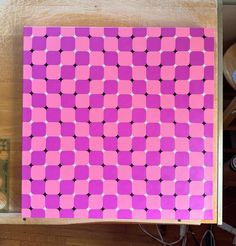 a pink and purple piece of art sitting on top of a wooden table