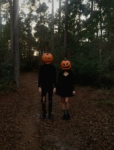 two people wearing pumpkin heads walking down a path in the woods with trees behind them