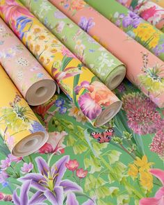 several rolls of colorful floral wrapping paper on a green tablecloth with pink, yellow and purple flowers