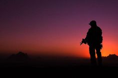 the silhouette of a man standing on top of a hill at sunset with mountains in the background