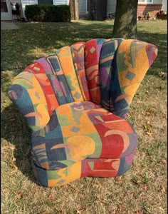 a multicolored chair sitting in the grass near a tree and some houses behind it