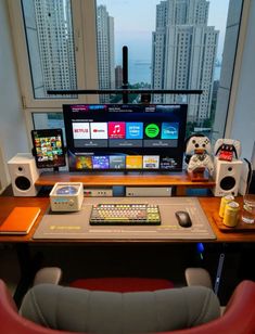 a desk with a computer, keyboard and speakers in front of a large window overlooking the city