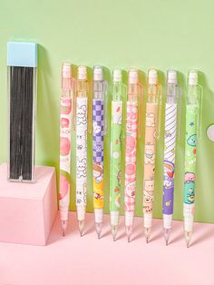 several pens are lined up next to each other on a pink surface with a green wall in the background