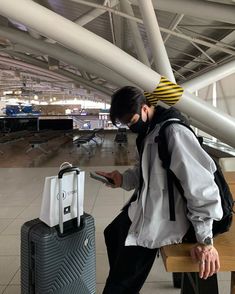 a man sitting on a bench looking at his cell phone while holding a suitcase in front of him