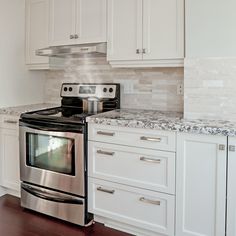 a stove top oven sitting inside of a kitchen next to white cabinets and counter tops