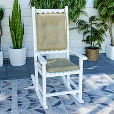 a white rocking chair sitting on top of a blue rug next to potted plants