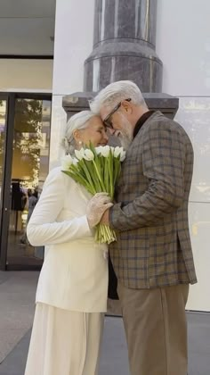 an older couple kissing each other in front of a statue