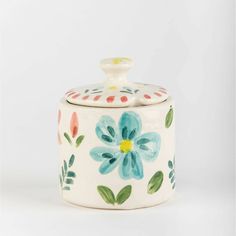 a ceramic container with flowers painted on the front and bottom, sitting against a white background