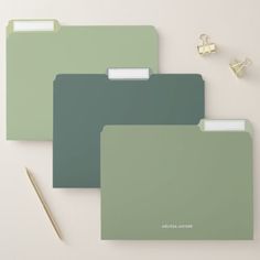 three green folders sitting on top of a table next to a pen and pencil