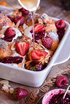 a person pouring syrup on some fruit in a white casserole with almonds and raspberries