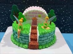 a birthday cake with tinkerbells sitting on top of grass and a brick wall