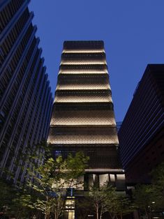 the tall building is lit up at night in front of other skyscrapers and trees