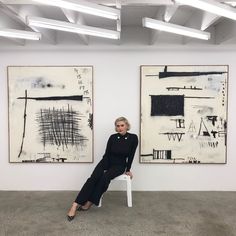 a woman is sitting on a chair in front of two abstract paintings, one black and white