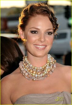 a woman with a necklace and pearls on her neck smiles at the camera while standing in front of a crowd