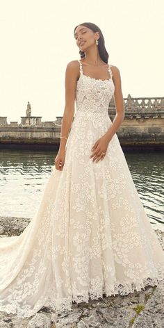 a woman in a white wedding dress standing on rocks near the water with her hand on her hip