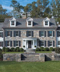 a large stone house with black shutters and white trim on the front door is shown