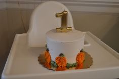 a first birthday cake decorated with pumpkins and leaves on a white tray in a bathroom