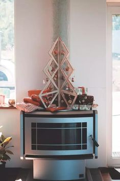 a small christmas tree is on top of a stand in front of a window with presents