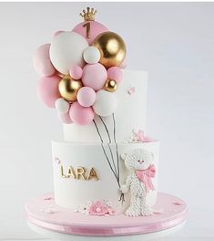 a white and pink cake with balloons on top