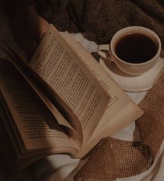 an open book sitting on top of a bed next to a cup of coffee