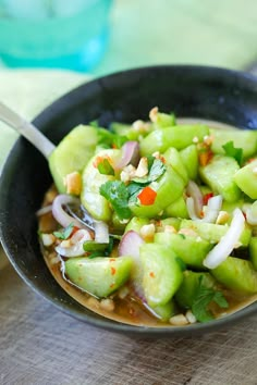 a black bowl filled with cucumber and onions on top of a wooden table