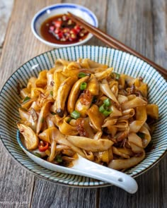 a bowl filled with noodles and vegetables next to chopsticks on a wooden table