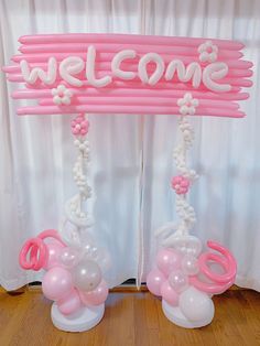 pink and white welcome sign with balloons attached to it