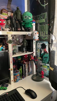 a desk with a computer monitor, keyboard and toy figures on it's shelves