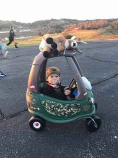 a young boy driving a toy car with stuffed animals on it's top and sides