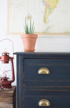 a blue dresser with a potted plant on top and an old map hanging above it