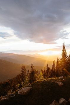 the sun is setting in the mountains with rocks and trees