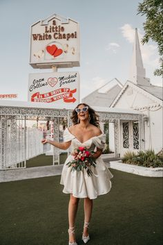 a woman standing in front of a little white chapel with her hand out to the side